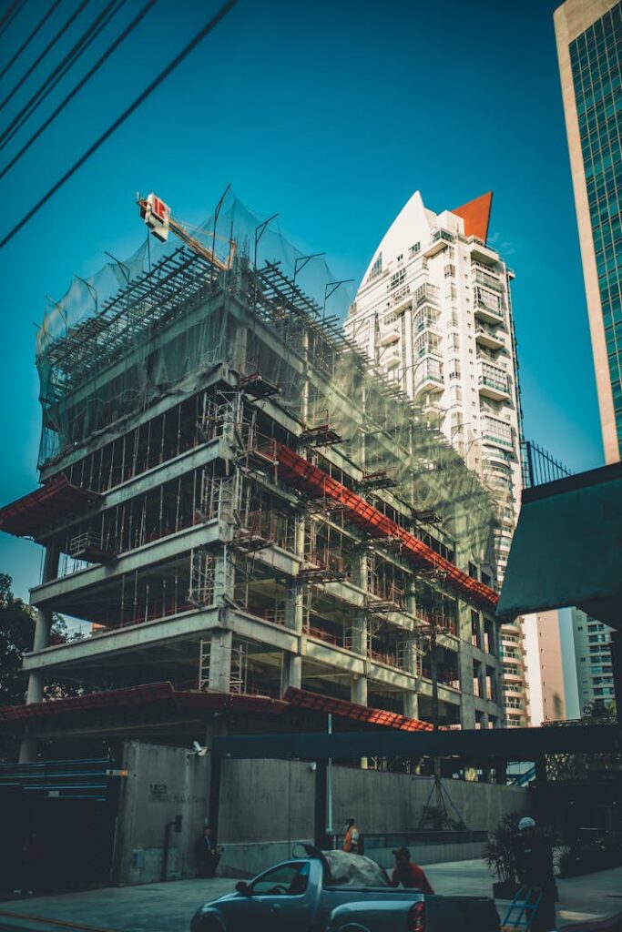 High-rise building under construction with scaffolding and crane in urban cityscape.